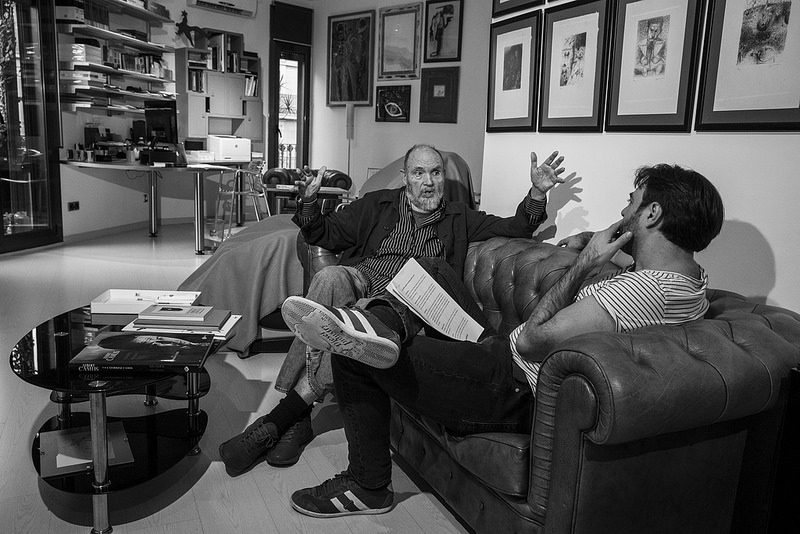 Ángel Alonso conversa assegut amb dues persones en una sala amb quadres emmarcats i una taula baixa plena de papers